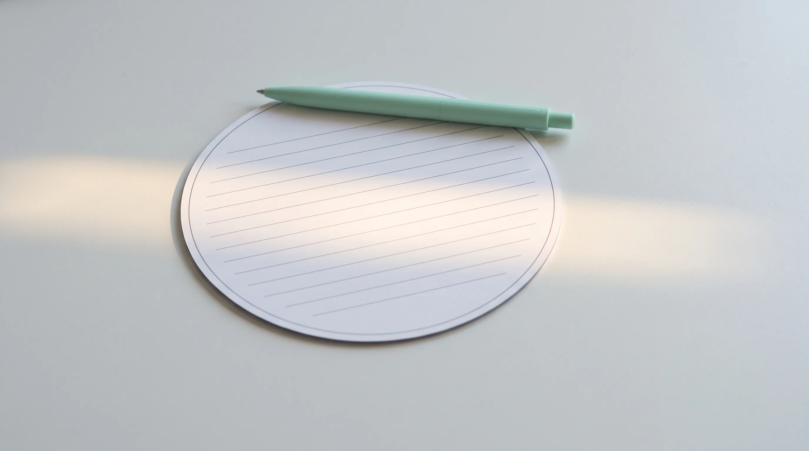 Blank ruled round-card form beside a mint pen on a clean worktop in raking morning light